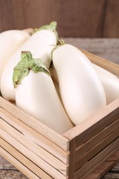 Fresh white eggplants in wooden crate on table, closeup