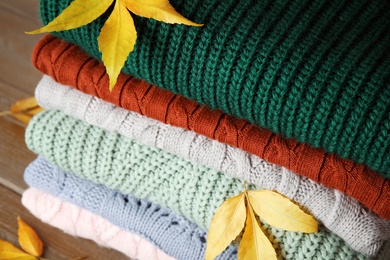 Photo of Stack of warm knitted clothes and autumn leaves on wooden background, closeup