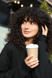 Photo of Happy young woman in stylish black sweater with cup of coffee outdoors