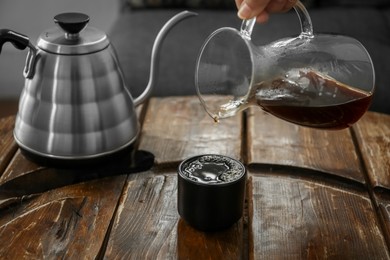 Photo of Barista pouring coffee into cup at wooden table in cafe, closeup