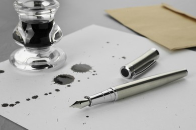 Photo of Stylish fountain pen, paper with blots of ink and inkwell on light grey table