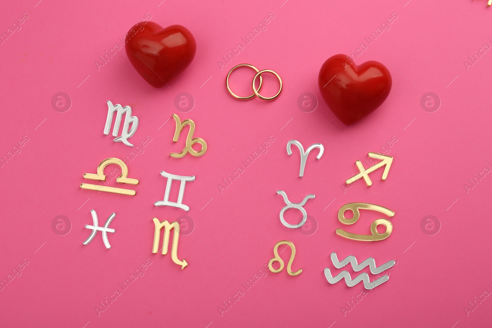 Photo of Zodiac compatibility. Signs, wedding rings and red hearts on pink background, flat lay