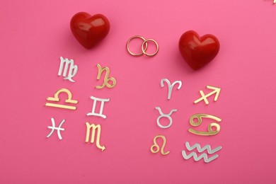 Photo of Zodiac compatibility. Signs, wedding rings and red hearts on pink background, flat lay