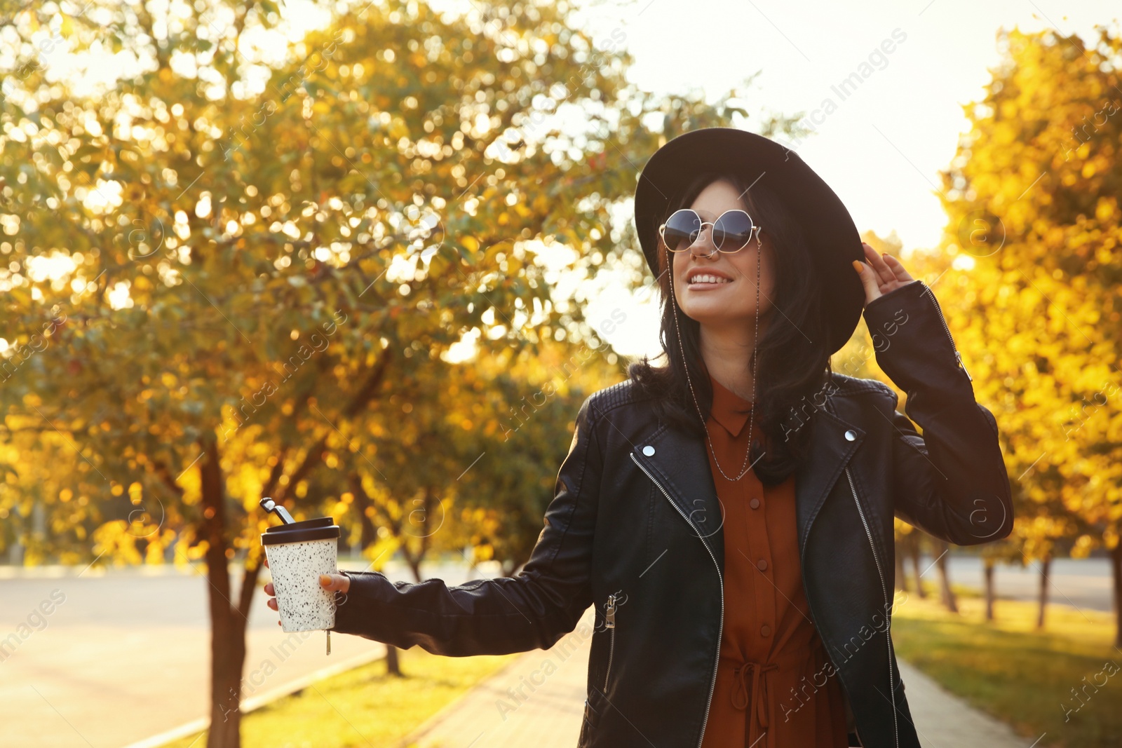 Photo of Beautiful young woman with cup of coffee wearing stylish clothes in autumn park