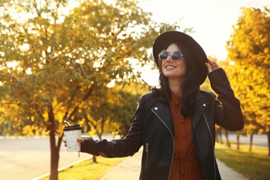 Beautiful young woman with cup of coffee wearing stylish clothes in autumn park