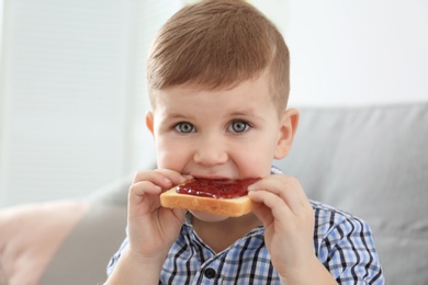 Cute little boy eating toast with sweet jam at home