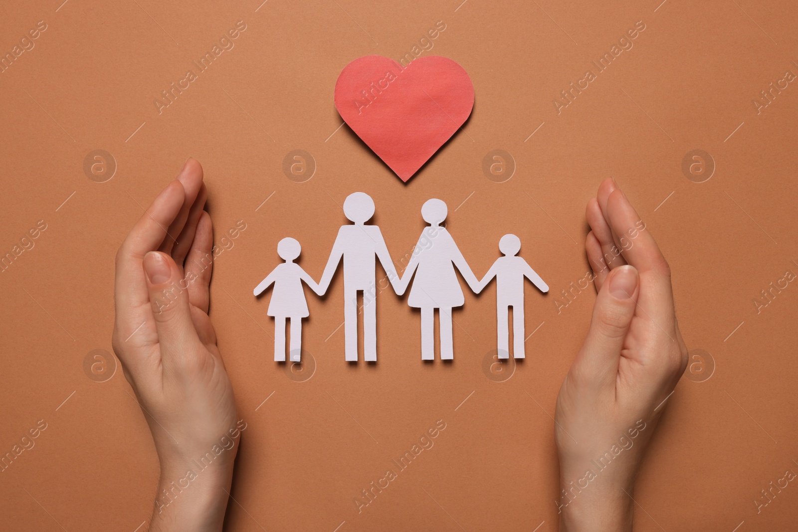 Photo of Woman protecting paper family figures and red heart on brown background, top view. Insurance concept