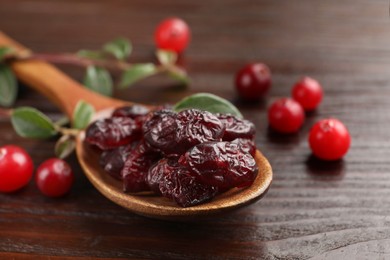 Photo of Tasty dried cranberries in spoon and fresh ones on wooden table, closeup