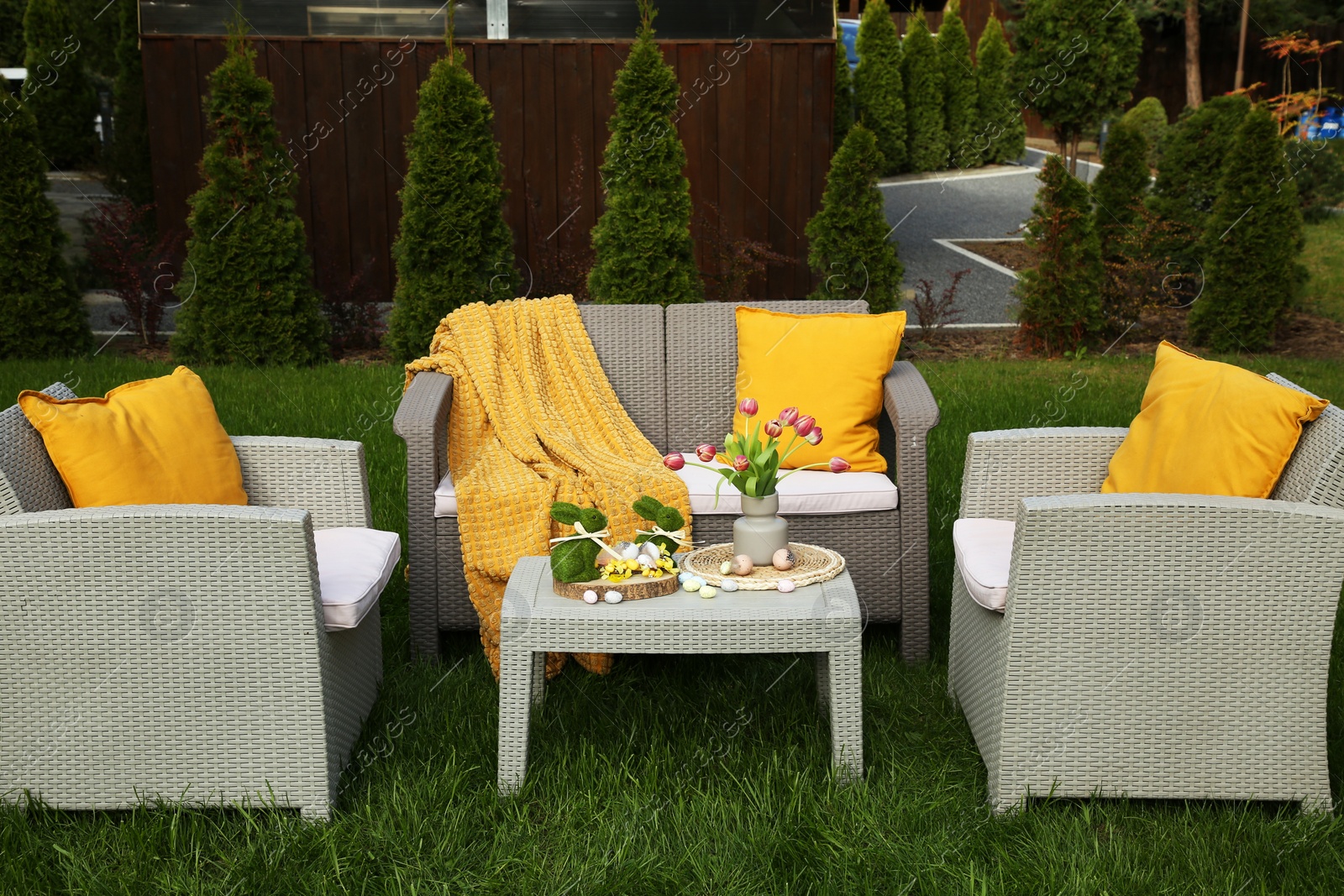 Photo of Easter decorations. Bouquet of tulips in vase, bunny figures and decorated eggs on table in backyard