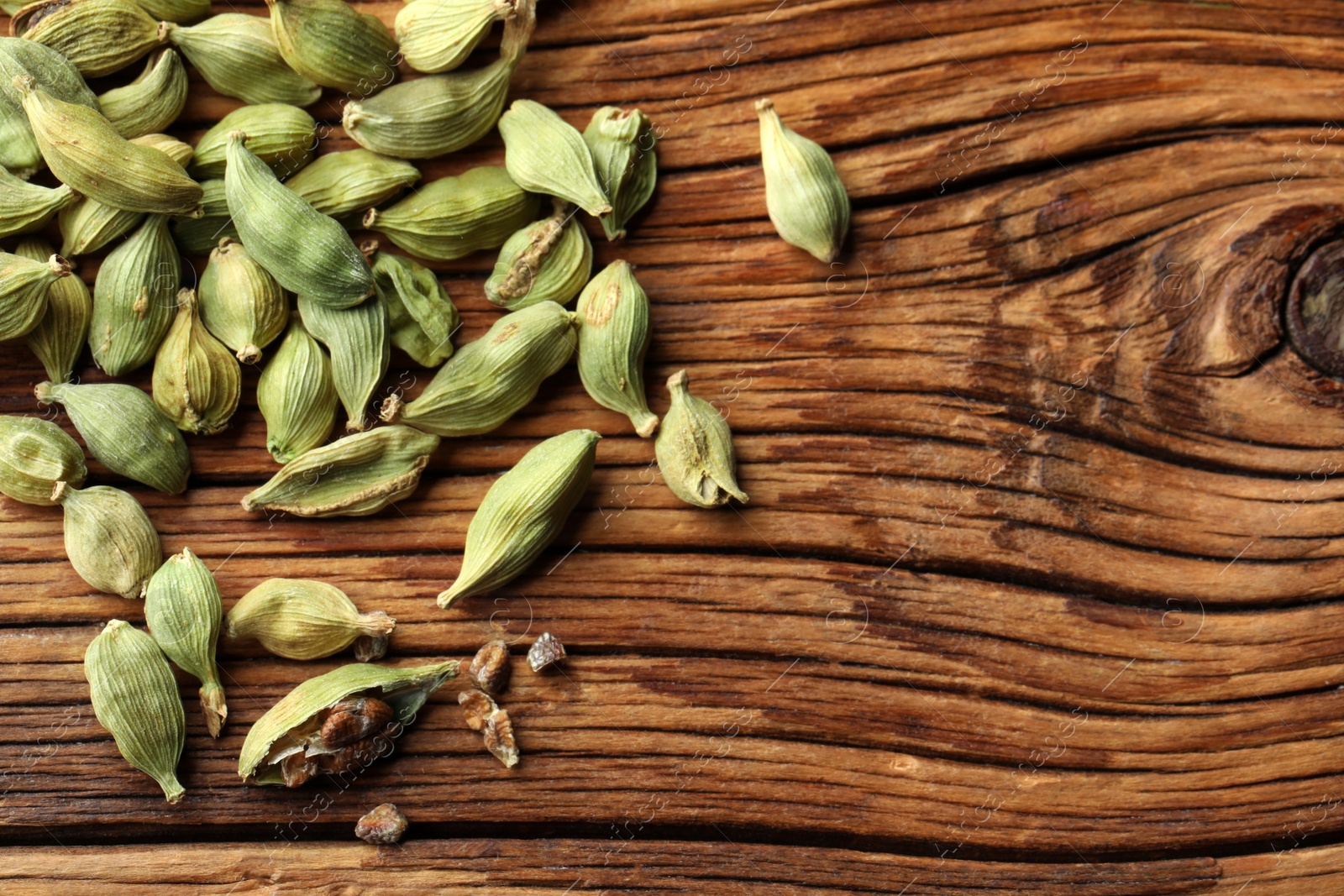 Photo of Pile of dry cardamom pods on wooden table, top view. Space for text