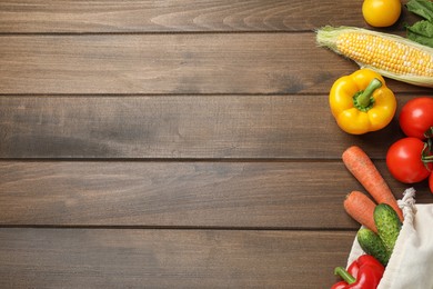 Cloth bag with fresh vegetables on wooden table, flat lay. Space for text