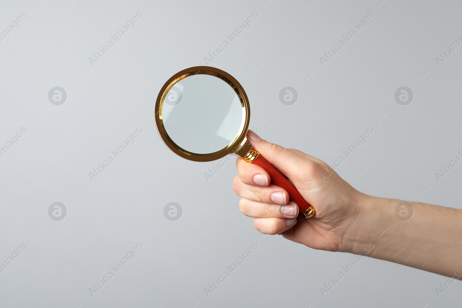 Photo of Woman holding magnifying glass on grey background, closeup. Find keywords concept