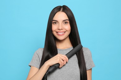 Photo of Beautiful happy woman using hair iron on light blue background