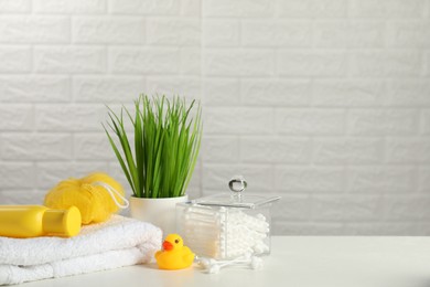 Photo of Baby cosmetic product, bath duck, cotton swabs and towel on white table against brick wall. Space for text
