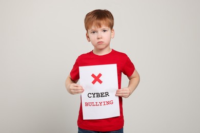 Photo of Boy holding sign with phrase Cyber Bullying on light grey background