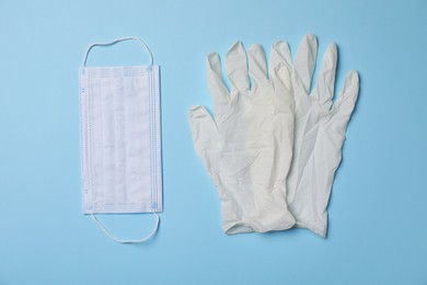 Medical gloves and protective mask on light blue background, flat lay. Safety equipment