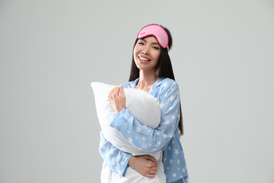 Beautiful Asian woman with pillow on light grey background. Bedtime