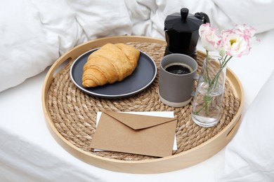 Photo of Tray with tasty croissant, cup of coffee and flowers on white bed
