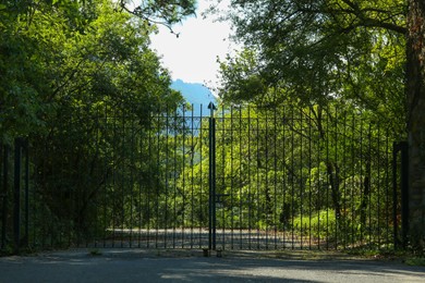 Big black gates near trees outdoors on sunny day