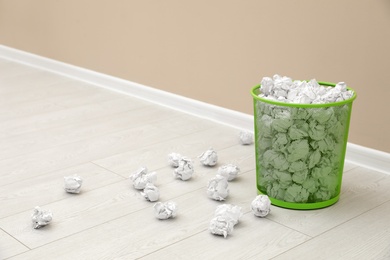 Photo of Metal bin and crumpled paper on floor near color wall, space for text