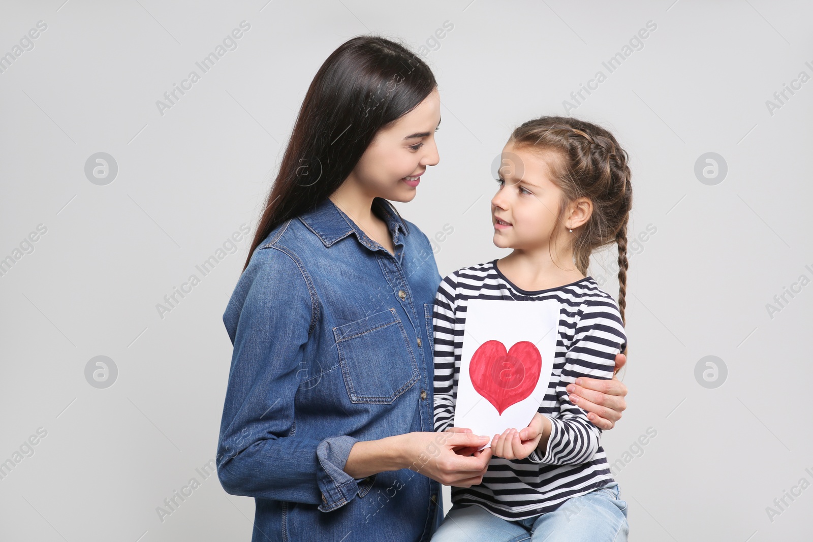 Photo of Happy woman with her daughter and handmade greeting card on light grey background. Mother's day celebration