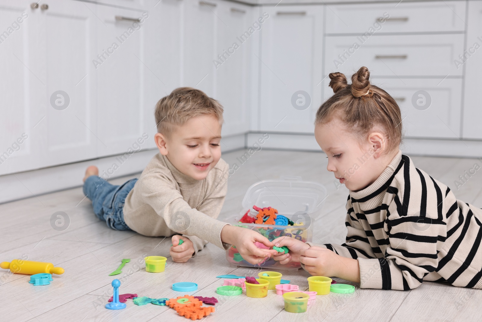 Photo of Cute little children playing together on warm floor in kitchen. Heating system