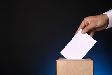 Man putting his vote into ballot box on dark blue background, closeup. Space for text