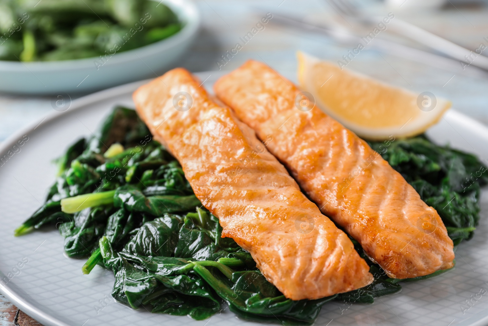 Photo of Tasty salmon with spinach and lemon on plate, closeup