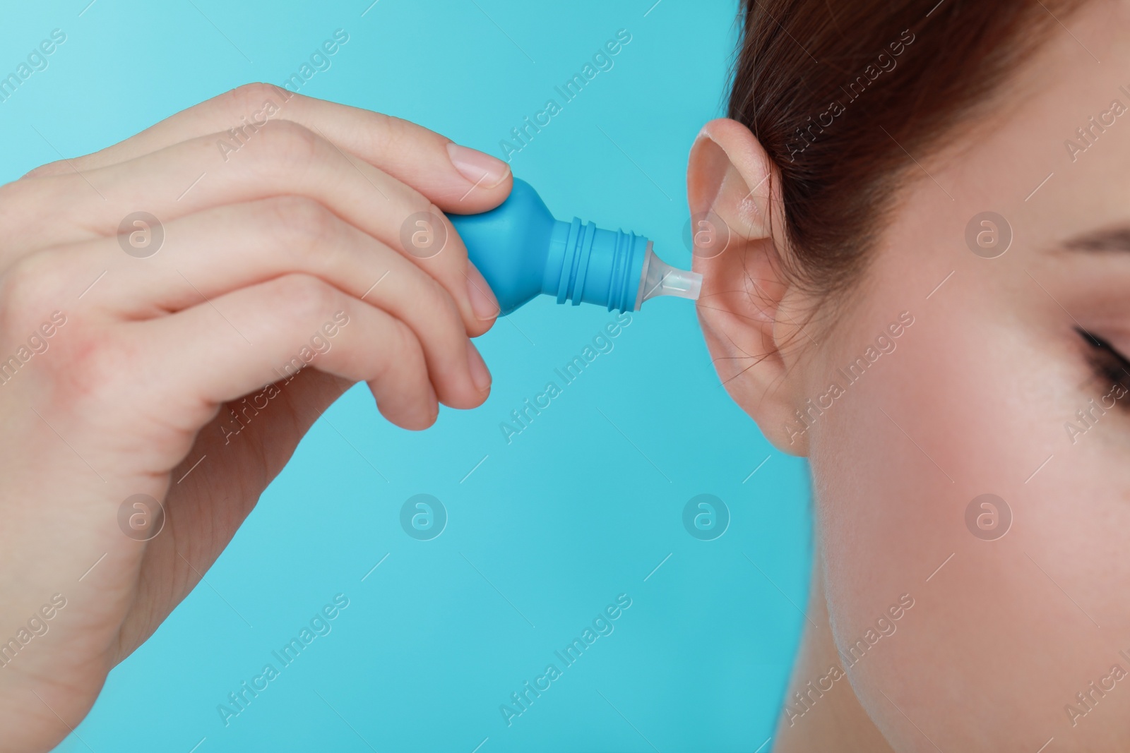 Photo of Woman using ear drops on light blue background, closeup