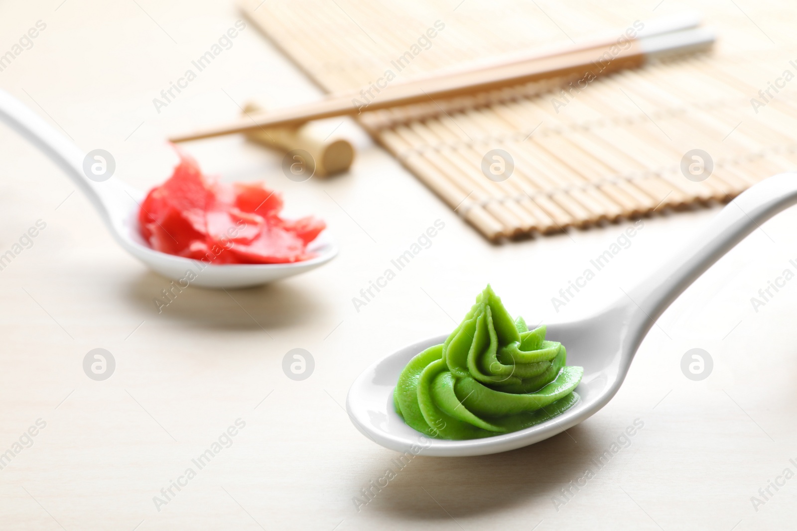 Photo of Spoons with swirl of wasabi paste and pickled ginger on white table, closeup