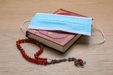 Photo of Muslim prayer beads, Quran and medical mask on wooden table