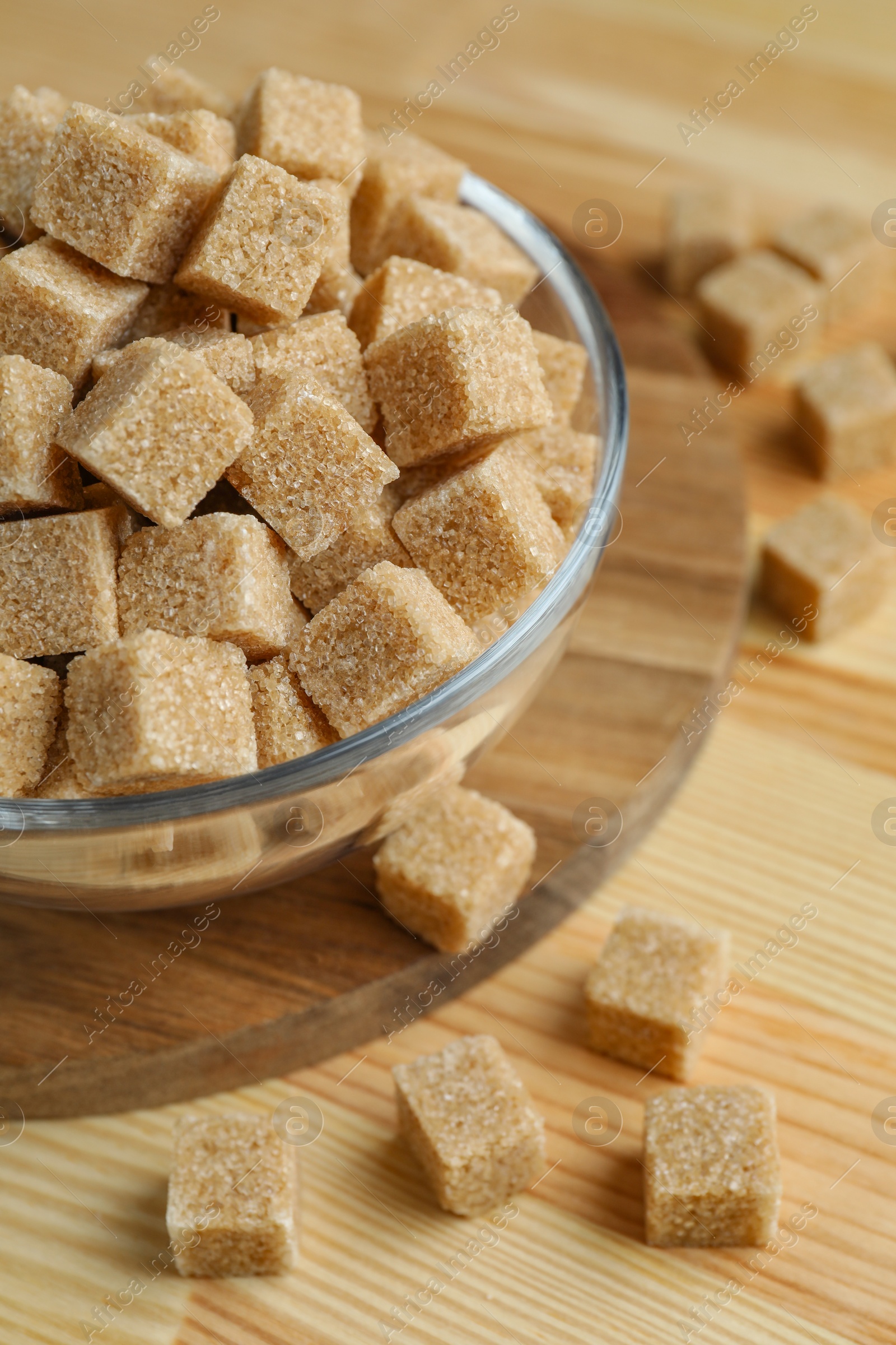 Photo of Brown sugar cubes in bowl on wooden table, closeup