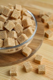 Photo of Brown sugar cubes in bowl on wooden table, closeup