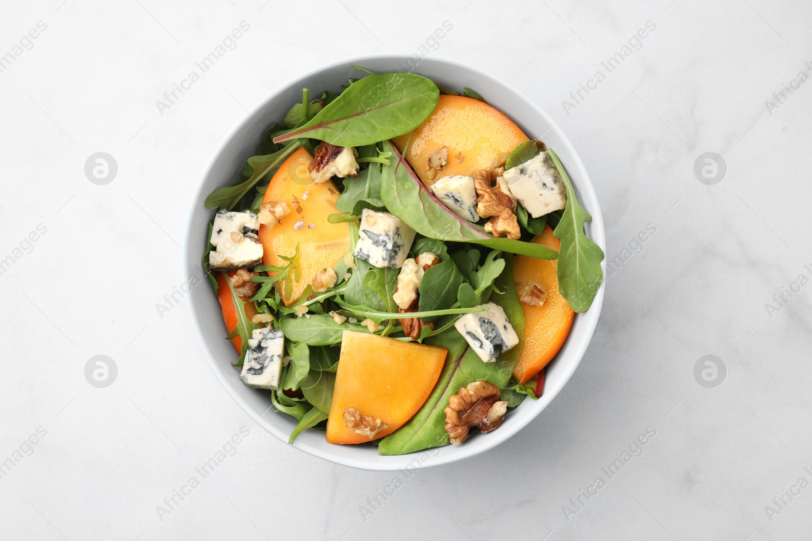 Photo of Tasty salad with persimmon, blue cheese and walnuts served on white marble table, top view