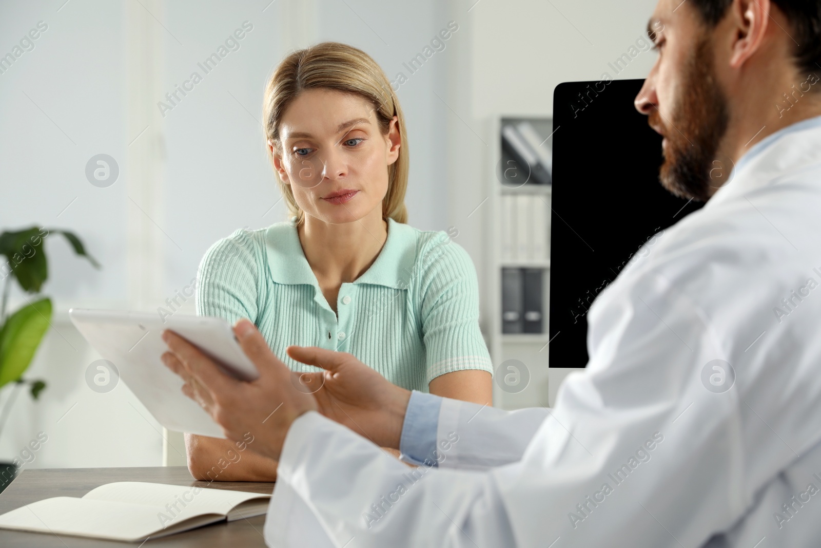 Photo of Doctor consulting patient at wooden table in clinic