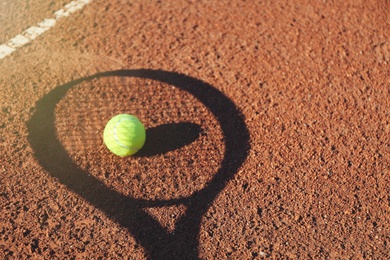 Photo of Shadow of racket and tennis ball on clay court. Space for text