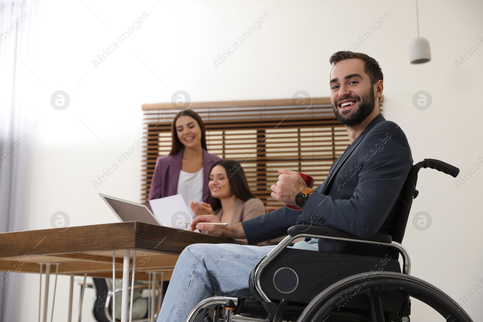 Photo of Young man in wheelchair with colleagues at workplace