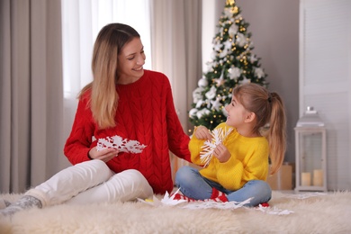 Photo of Happy mother and daughter making paper snowflakes near Christmas tree at home
