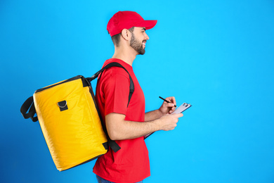 Courier with thermo bag and clipboard on light blue background, space for text. Food delivery service