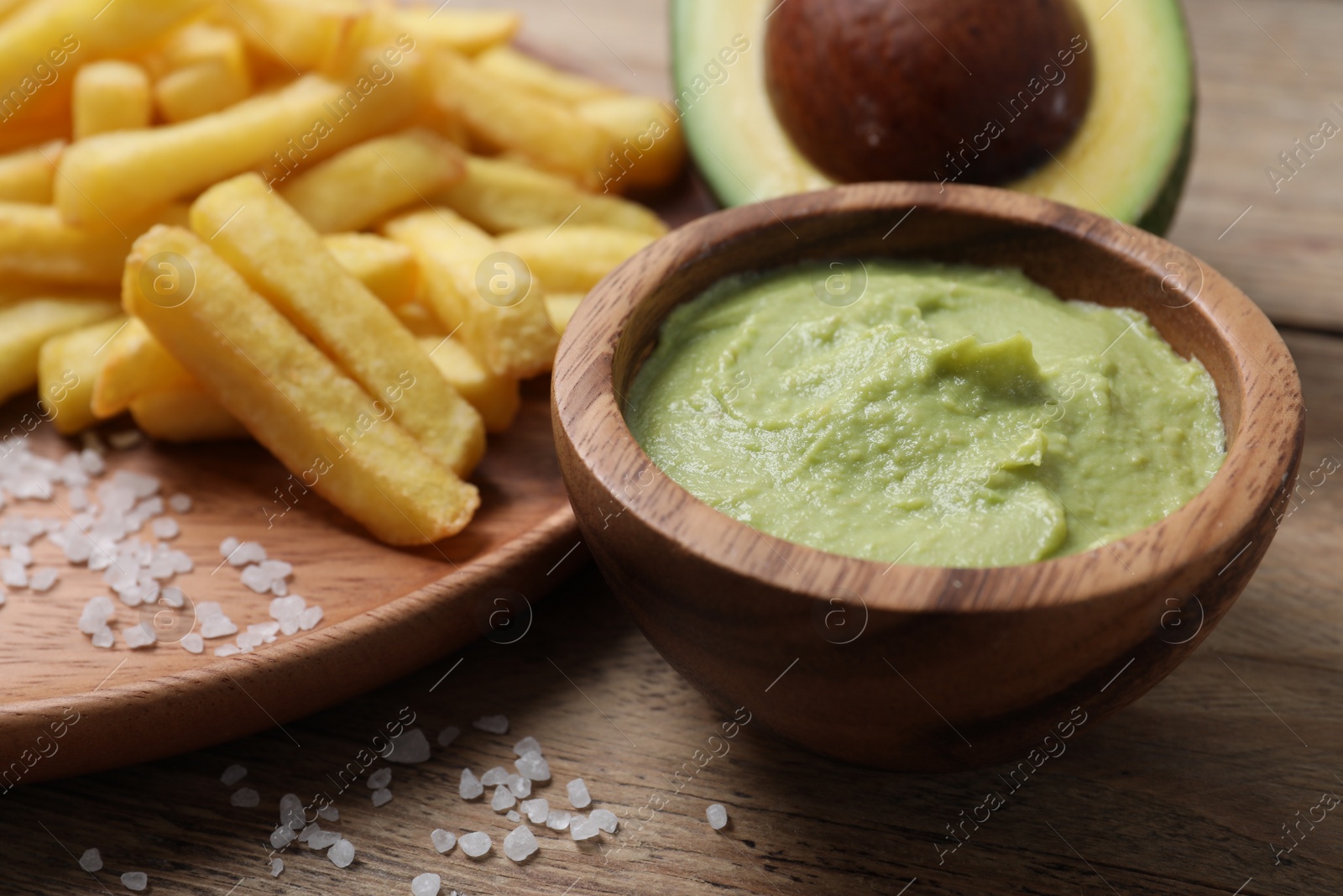 Photo of Plate with french fries, guacamole dip and avocado served on wooden table, closeup