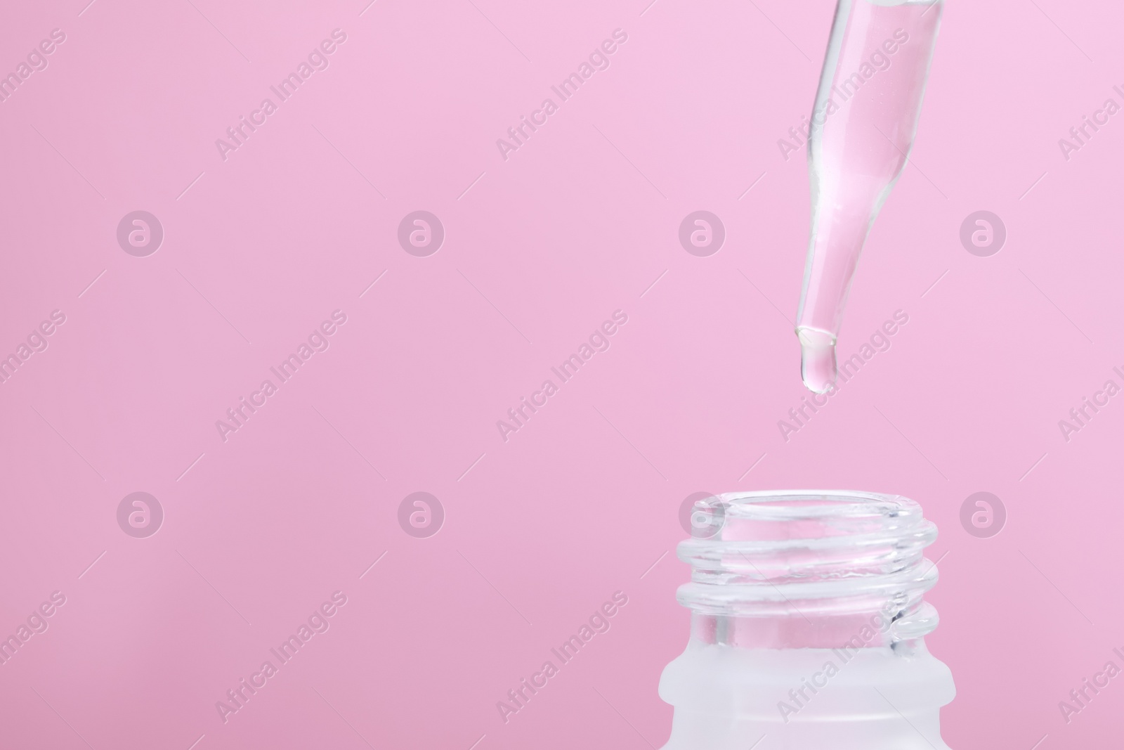 Photo of Dripping serum from pipette into bottle on pink background, closeup. Space for text
