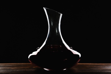 Photo of Elegant decanter with red wine on table against dark background