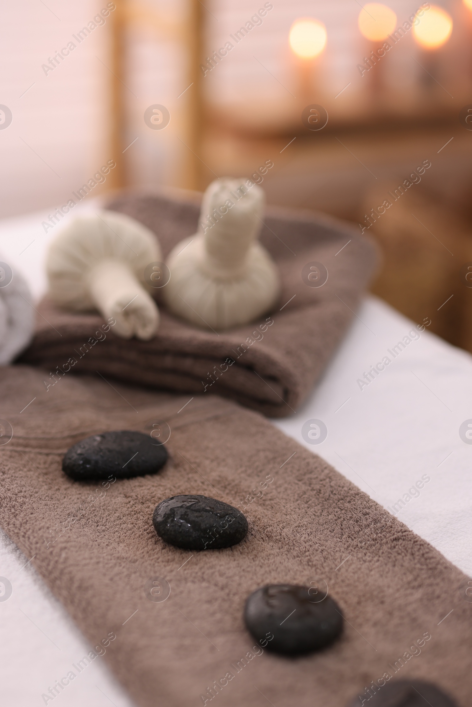 Photo of Towel with arranged spa stones and herbal bags on massage table in recreational center, closeup