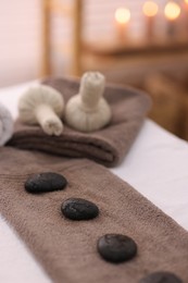 Towel with arranged spa stones and herbal bags on massage table in recreational center, closeup