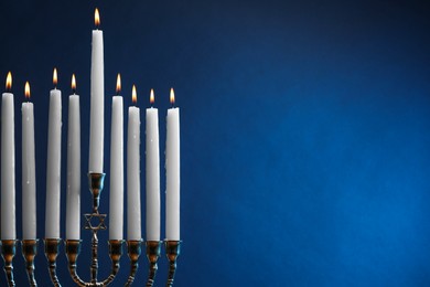Photo of Hanukkah celebration. Menorah with burning candles on blue background, space for text