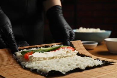 Chef in gloves making sushi roll at table, closeup