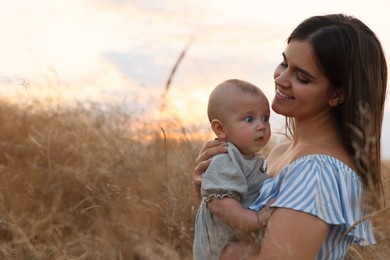 Happy mother with adorable baby in field at sunset, space for text