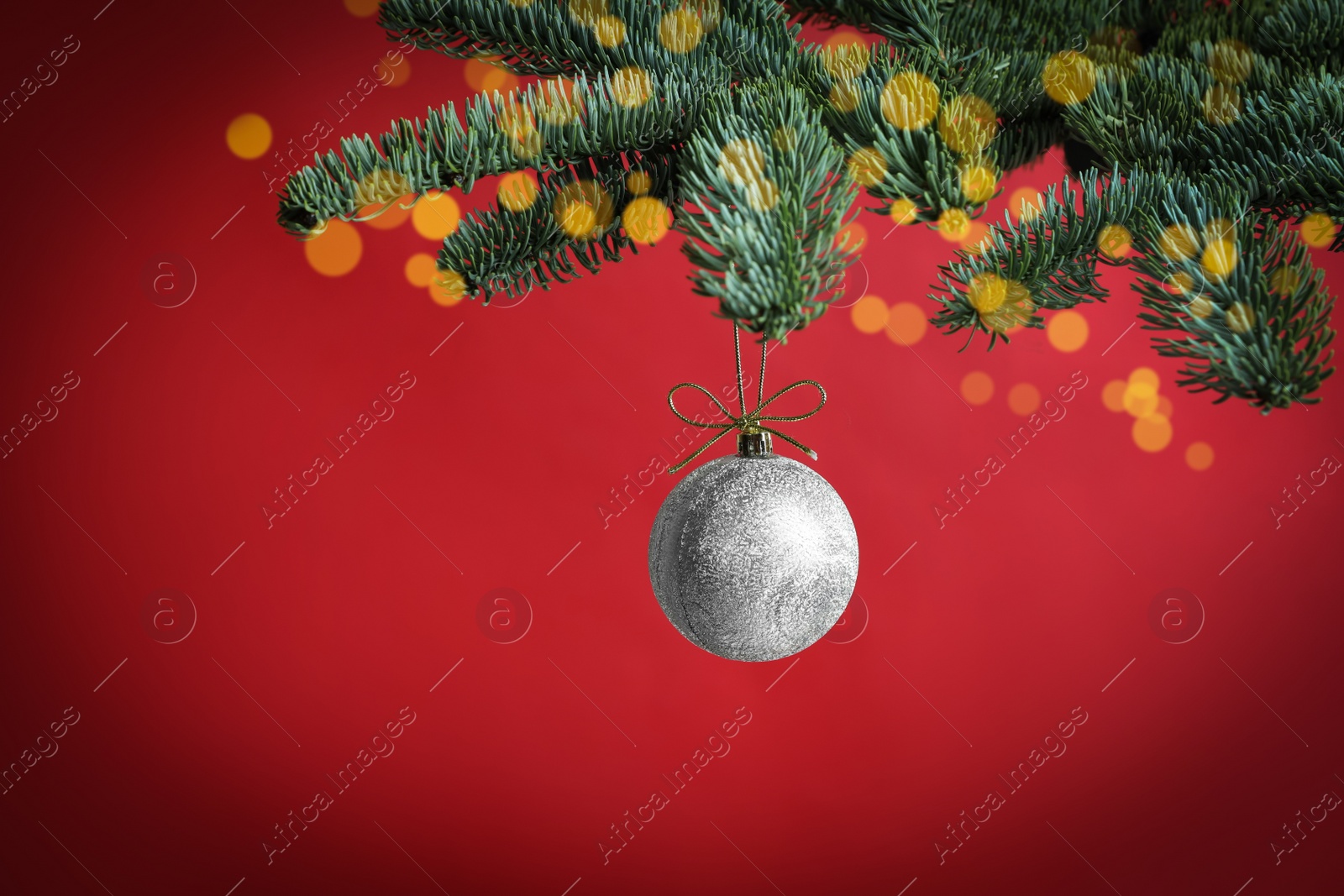 Photo of Beautiful Christmas ball hanging on fir tree branch against red background, bokeh effect