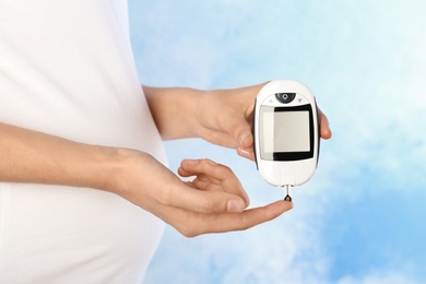 Pregnant woman checking blood sugar level with glucometer on color background. Diabetes test