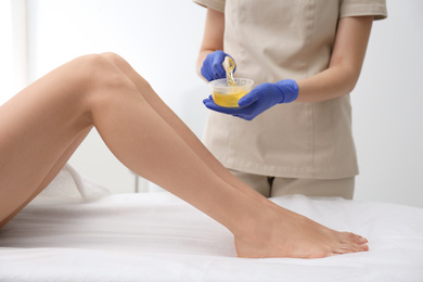 Photo of Woman getting wax epilation of legs in salon, closeup